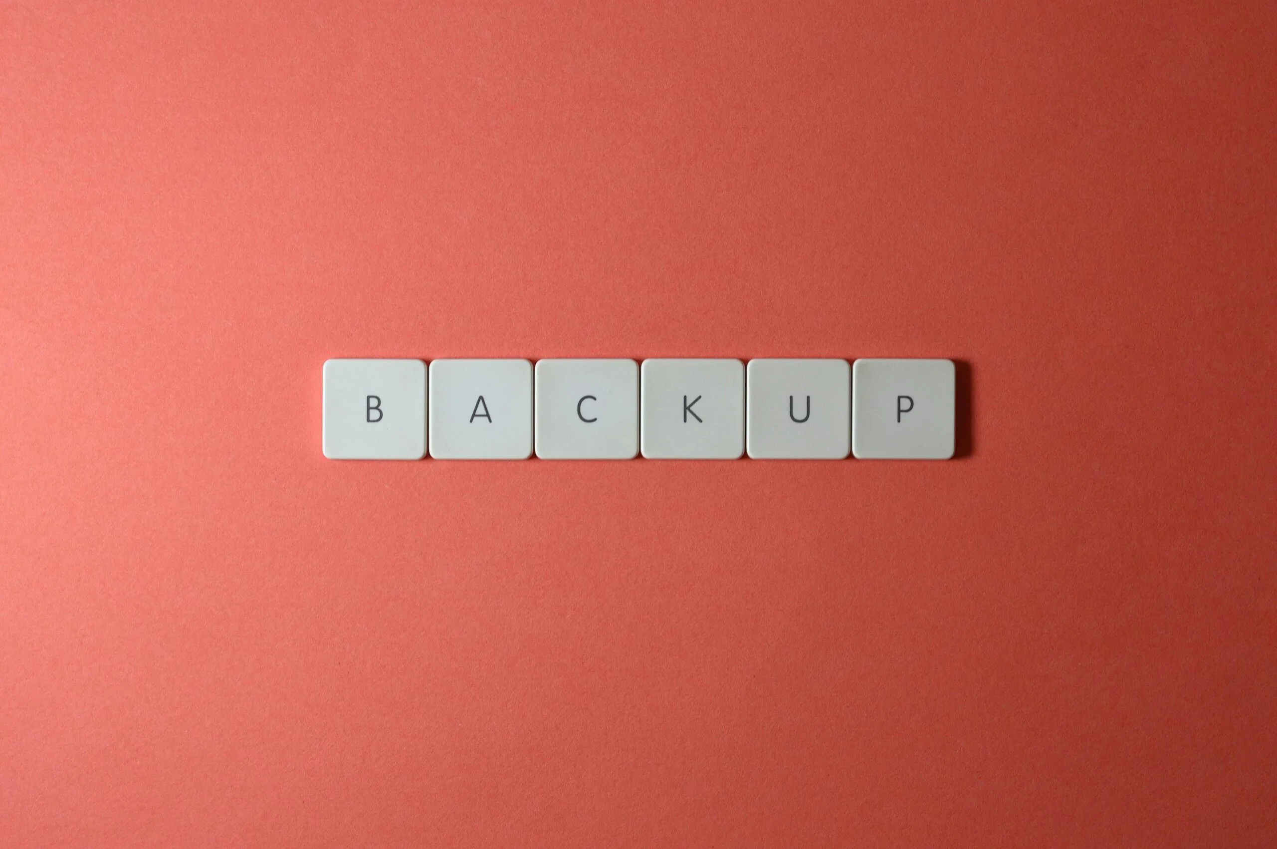 Free Close-up of keyboard keys spelling 'BACKUP' placed on a coral-colored surface. Stock Photo